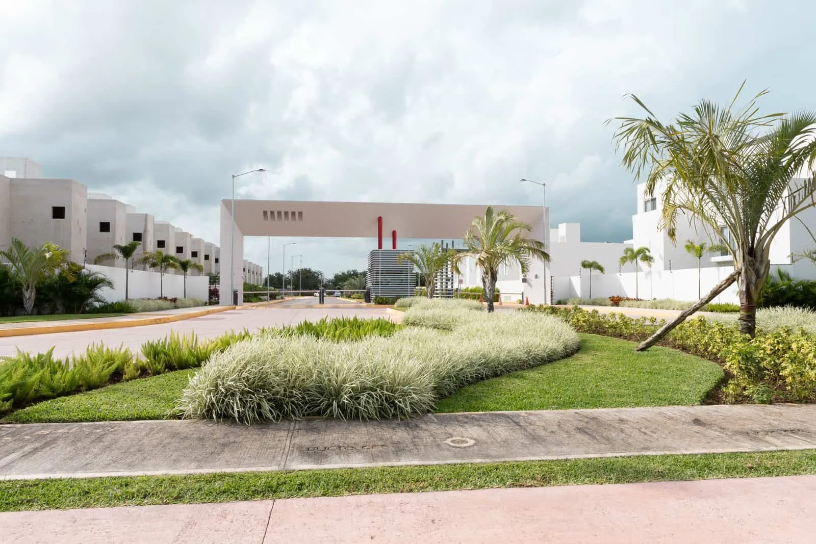 Acceso principal de Jardines del Sur 6 en Cancún, con la caseta de vigilancia, las palmeras y las casas ya terminadas